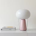 Modern Table Lamp With White Spherical Lampshade Pink Base And Metal Stand Next To Books
