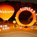 Illuminated Art Installation With Orange Hot Air Balloon Welcome Sign And Sunset Ring At Nighttime