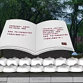 Red Open Book Sculpture with Text Surrounded by Green Plants and Bushes