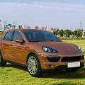 Orange Porsche SUV Parked On Green Grass Field With Modern Exterior Design And City Background