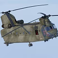 Military Green Twin Rotor Helicopter Flying In Blue Sky With Rotor Blades