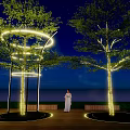 Illuminated Arbor Trees With Circular Lights On Night Wooden Deck And Person In White Dress