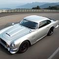 Silver Vintage Style Sports Car Parked On Race Track With Mountain Backdrop And Guardrail