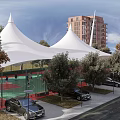 Tensile Membrane Structures Over Green Sports Court Near Red Brick Building With Trees And Cars
