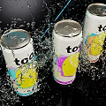 Three Colorful Too Drink Cans With Lemon Design Splashing Water And Blue Light