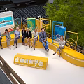 Group Sitting on Yellow Bench with Green Trees Blue Display Boards at New City University