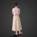 Woman in pink top and beige long skirt with crossed arms standing against gray background