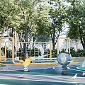 Green Children's Playground With Circular Curved Slides Swings Trees And Seating Areas
