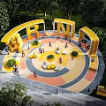 Public Park Landscape With Yellow RUN Sculptures Circular Colorful Ground Central Lawn Seats And Trees