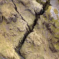 Scenic Mountainous Terrain With Flowing Stream Yellowish Green Textured Slopes And Visible Cracks
