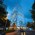 Tall Modern Office Building With Glass Curtain Wall Illuminated Evening Trees And Streetlights