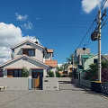 Detached Villa With White Exterior Brown Roof Paved Road And Trees Under Blue Sky