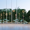 Outdoor Spherical Sculpture With Golden WELCOME Letters Wavy Decorations And Green Trees Background