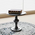 Black Round Top Side Table With Decorative Base And Books On Top On Round Rug