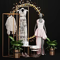 Mannequin Wearing Pink Asymmetrical Dress With Golden Display Rack Green Plants And Decorative Lights