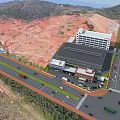 Aerial View Industrial Factory Building With Surrounding Roads Vehicles Red Soil Hills And Distant Mountains