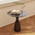 Modern Round Black Side Table with Open Book Stack and Glass Vase on Wooden Floor