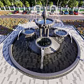 Ornate Fountain With Central Sculpture Water Flowing In Urban Plaza With Buildings And Greenery