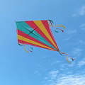 Colorful Triangular Kite Flying In Blue Sky With Colorful Streamers