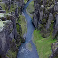 Scenic Canyon Landscape With River Flowing Through Moss Covered Rock Cliffs And Green Grass