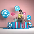 Girl In Yellow Top Sitting On Blue Red Striped Block With Colorful Lollipops And Megaphone