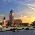 Red Brick School Building with Clock Tower Central Plaza Benches and Greenery Under Sunset Sky
