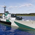 Green and White Warship on Blue Water with Masts and Distant Shore