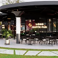 Modern Café With Curved Roof Glass Walls Outdoor Seating And Greenery Decor
