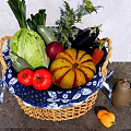 Fresh Assorted Vegetables in Wicker Basket with Blue and White Patterned Cloth on Gray Countertop
