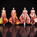 Four women in flowing orange and yellow gradient long dresses with reflections on black background