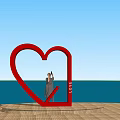 Red Heart Sculpture With LOVE Letters And Person Taking Photo Against Blue Sky And Sea