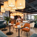Modern Café Interior With Blue Sofa Orange Chairs Round Tables Pendant Lights And Green Plants