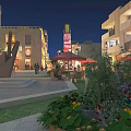 Vibrant Commercial Street At Night Featuring Illuminated Buildings Square Sculpture Outdoor Umbrellas Plants And Pedestrians
