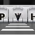 Person Standing By PVH Letters With White Brick Wall And Street Lamps Near Zebra Crossing