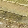 Outdoor Concrete Bench On Brick Pavement With Fallen Leaves And Snow Patches