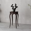 Dark Wooden Side Table With Carved Legs And Abstract Sculptural Vases By Green Plants