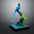 Blue Bird Sculpture Perched On Green Branch With Green Leaves And Blue Base