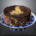 Chocolate Cake With Golden Cream Topping And Colorful Sprinkles On Blue And White Plate
