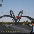 Modern Entrance Gate with Curved Arch Structure Featuring Logo Surrounded by Cars Pedestrians and Trees