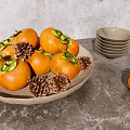 Fresh Persimmons in Brown Plate with Pine Cones Bowls and Clear Cups on Gray Tabletop