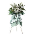 White Flower Arrangement With Green Leaves And Light Green Bow On Stand