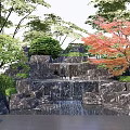Rockery Stones With Waterfall Red Maple And Lush Greenery In Garden Landscape