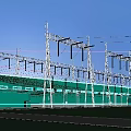 Green Industrial Factory Building With Metal Power Transmission Towers Under Blue Sky And Green Grassland