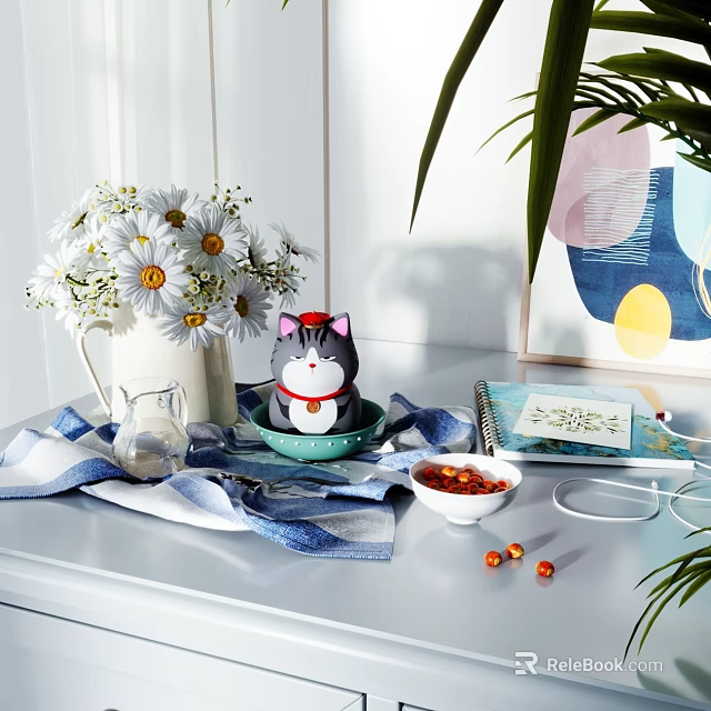 Decorative Ornament Collection with White Daisies Cat Figurine Blue Bowl Notebook and Striped Cloth on Table 3d model 