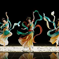 Women dancing in flowing costumes waving colorful ribbons on black background with shiny floor