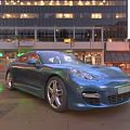 Blue Sports Car Parked On City Street With Tall Buildings And Evening Lights