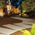 Nighttime Residential Garden Landscape With Curved Stone Walkway Lighting Greenery And Flower Beds