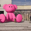 Large Pink Bear Sculpture Standing Outside Adidas Shopping Mall With Pedestrians