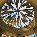 Ornate Circular Metal Ceiling With Leaf Patterns And Columns Against High Rise Buildings