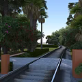 Railway Track And Stone Paved Road With Palm Trees Red Flowers Orange Pillars And Shrubs